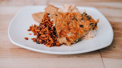 Delicious Indonesian tempeh dish with rice and crispy omelet on a white plate.