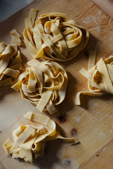 Nests of freshly cut egg tagliatelle dusted with flour on a pale wooden board
