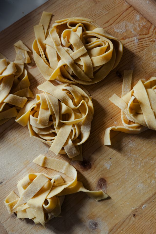 Nests of freshly cut egg tagliatelle dusted with flour on a pale wooden board