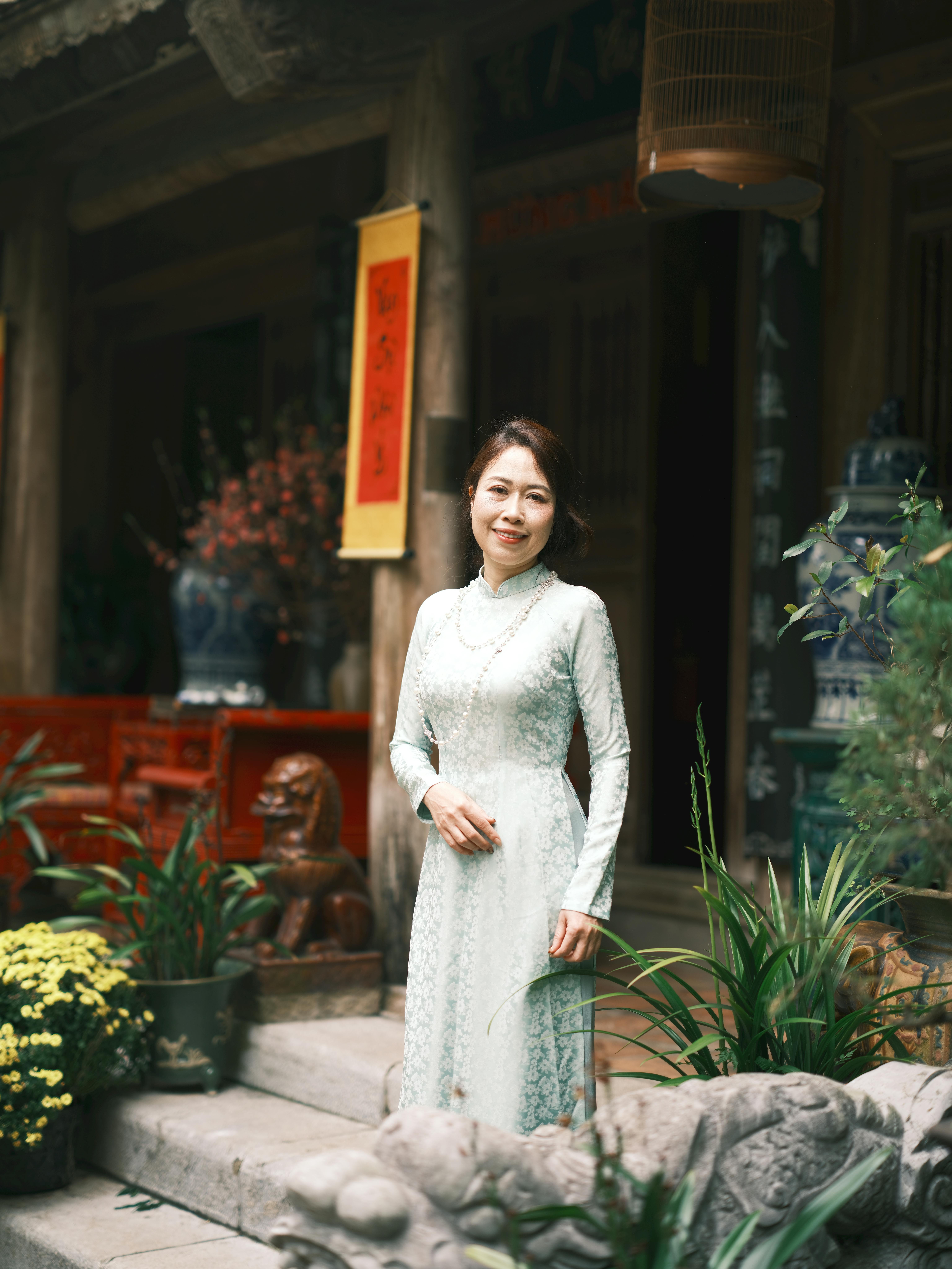 A woman wearing an Ao Dai stands gracefully at a Vietnamese temple entrance surrounded by lush greenery.