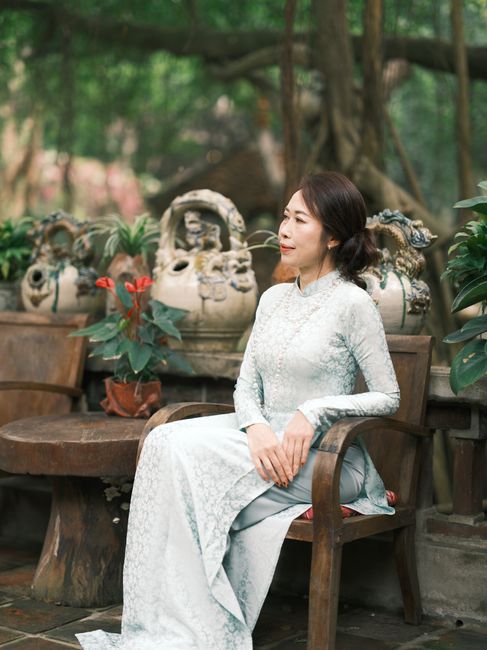 A serene portrait of a woman wearing a traditional white Ao Dai in a lush garden setting in Vietnam.