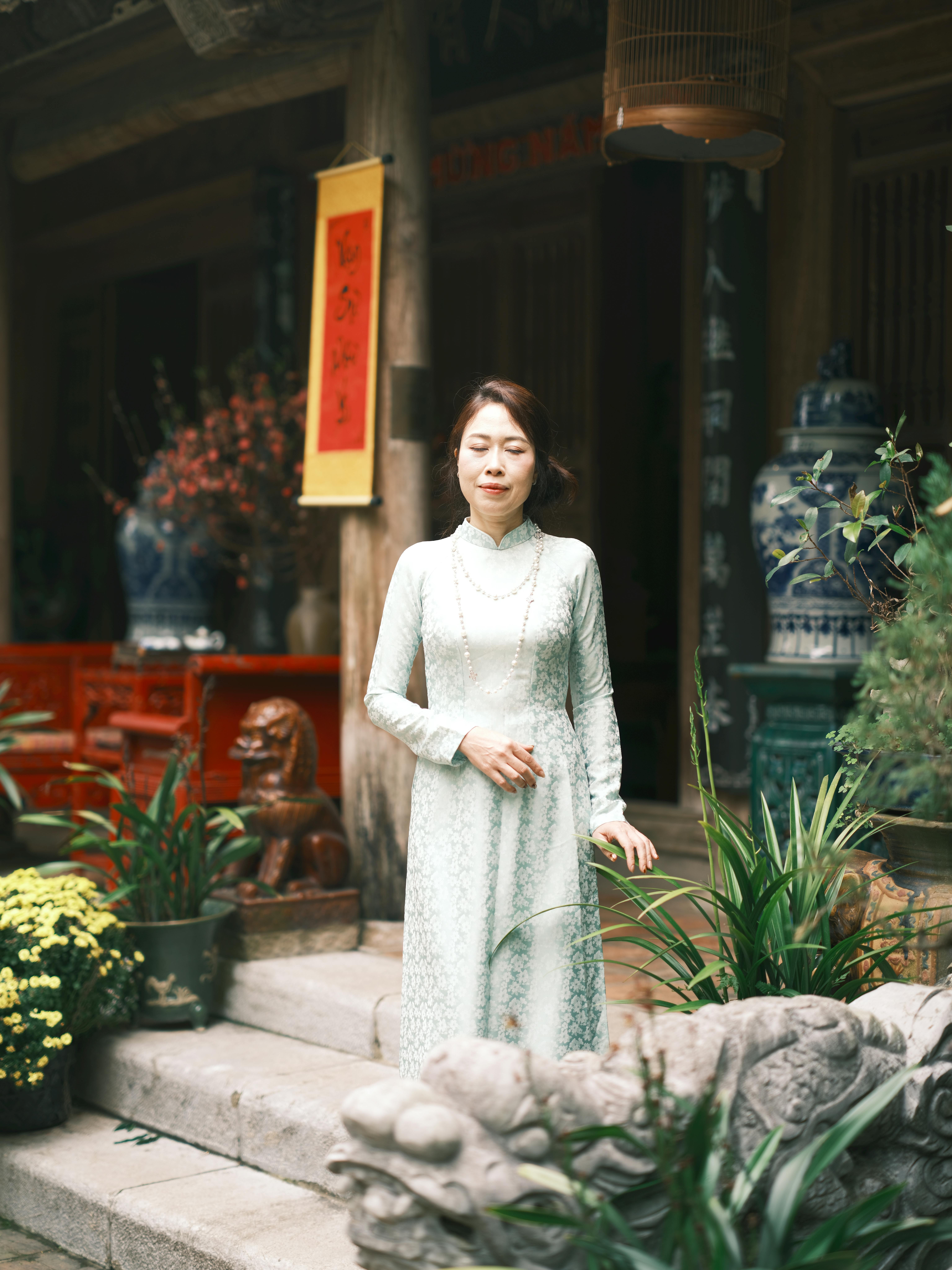 Portrait of a woman in traditional Vietnamese dress standing in a culturally rich courtyard.