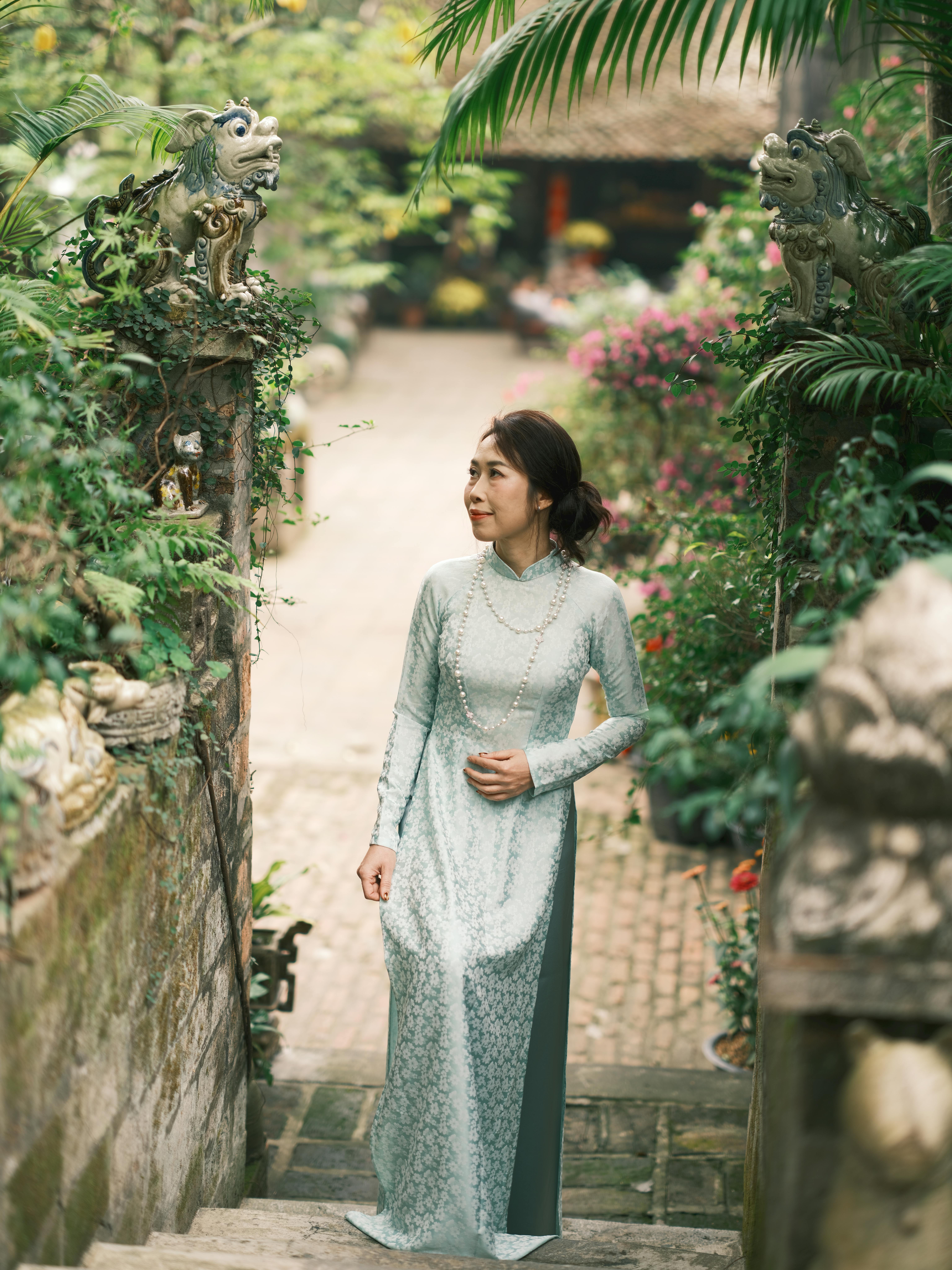 A woman in an elegant ao dai dress stands in a lush Vietnamese garden.