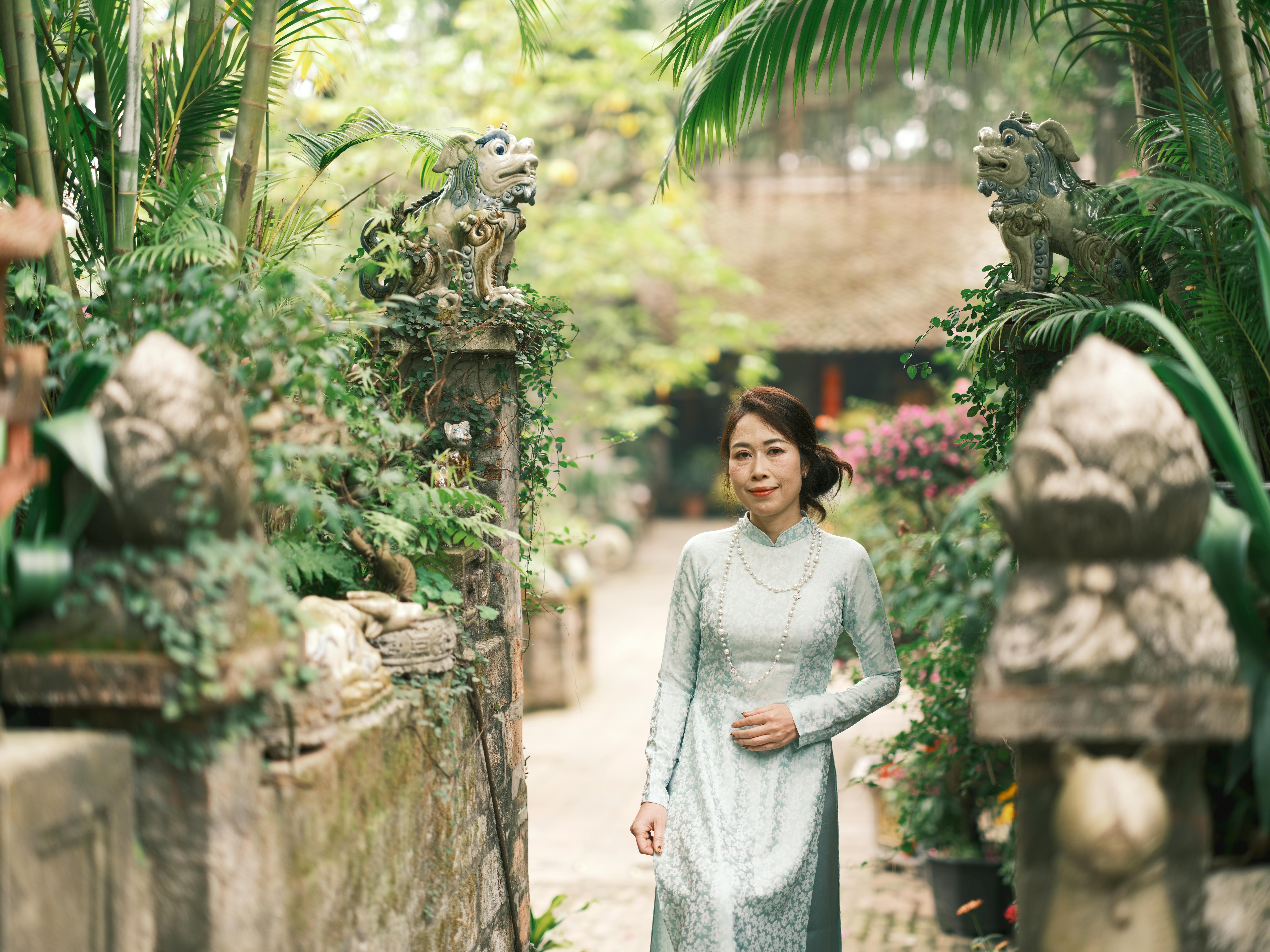 A woman in a traditional Ao Dai dress walks through a garden in Vietnam.