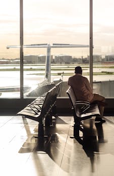 A man sits in an airport terminal, watching an airplane through the glass at sunset.