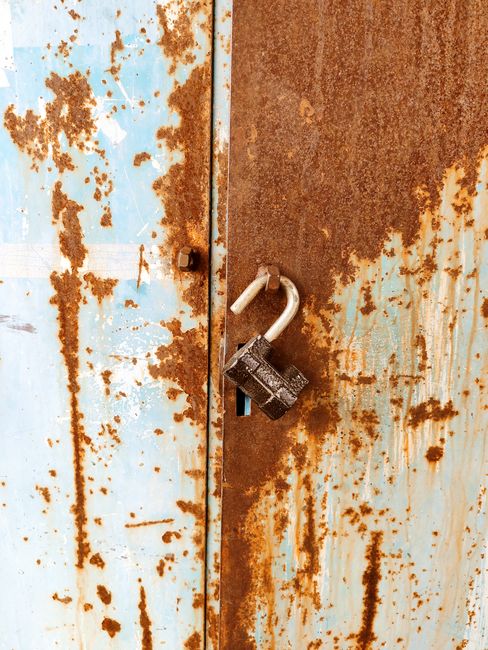 Fotomural Primer plano de un candado oxidado en una vieja puerta azul desgastada por el tiempo, con la pintura descascarada.