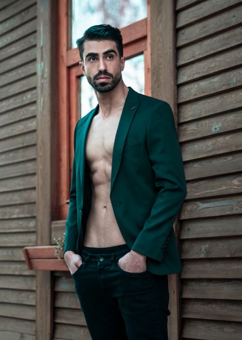 Free Confident male model posing in a blazer with hands in pockets against a wooden wall. Stock Photo