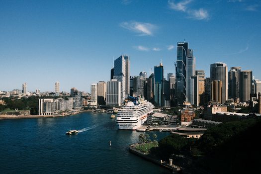 Aerial view of Sydney skyline with a cruise ship docked at the harbor under a clear blue sky.