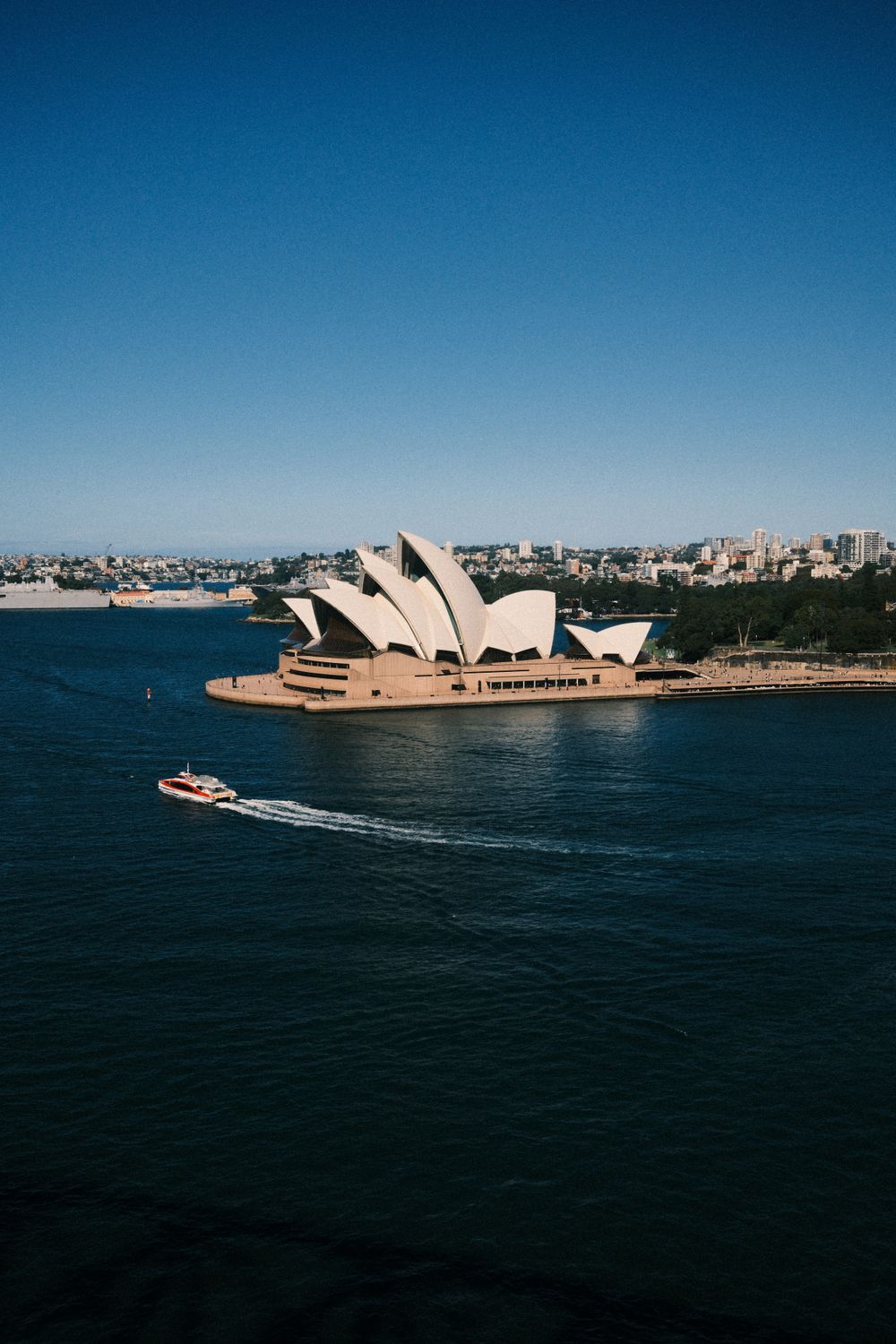 Vista elevada de la Sydney Opera House con ferry cruzando la bahía bajo cielo despejado