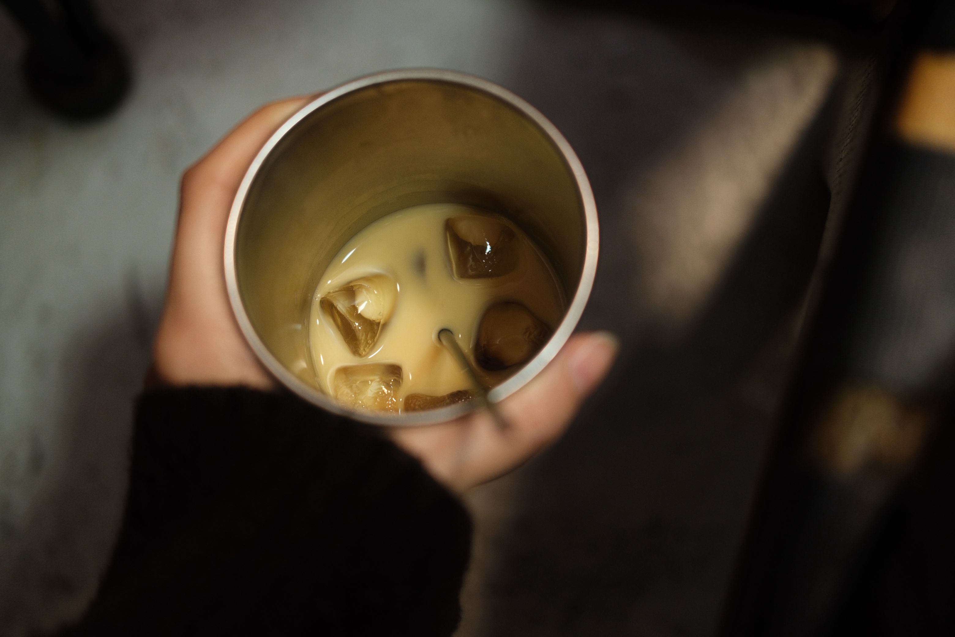 Hand holding a cup of iced coffee with milk, providing a cozy afternoon vibe.