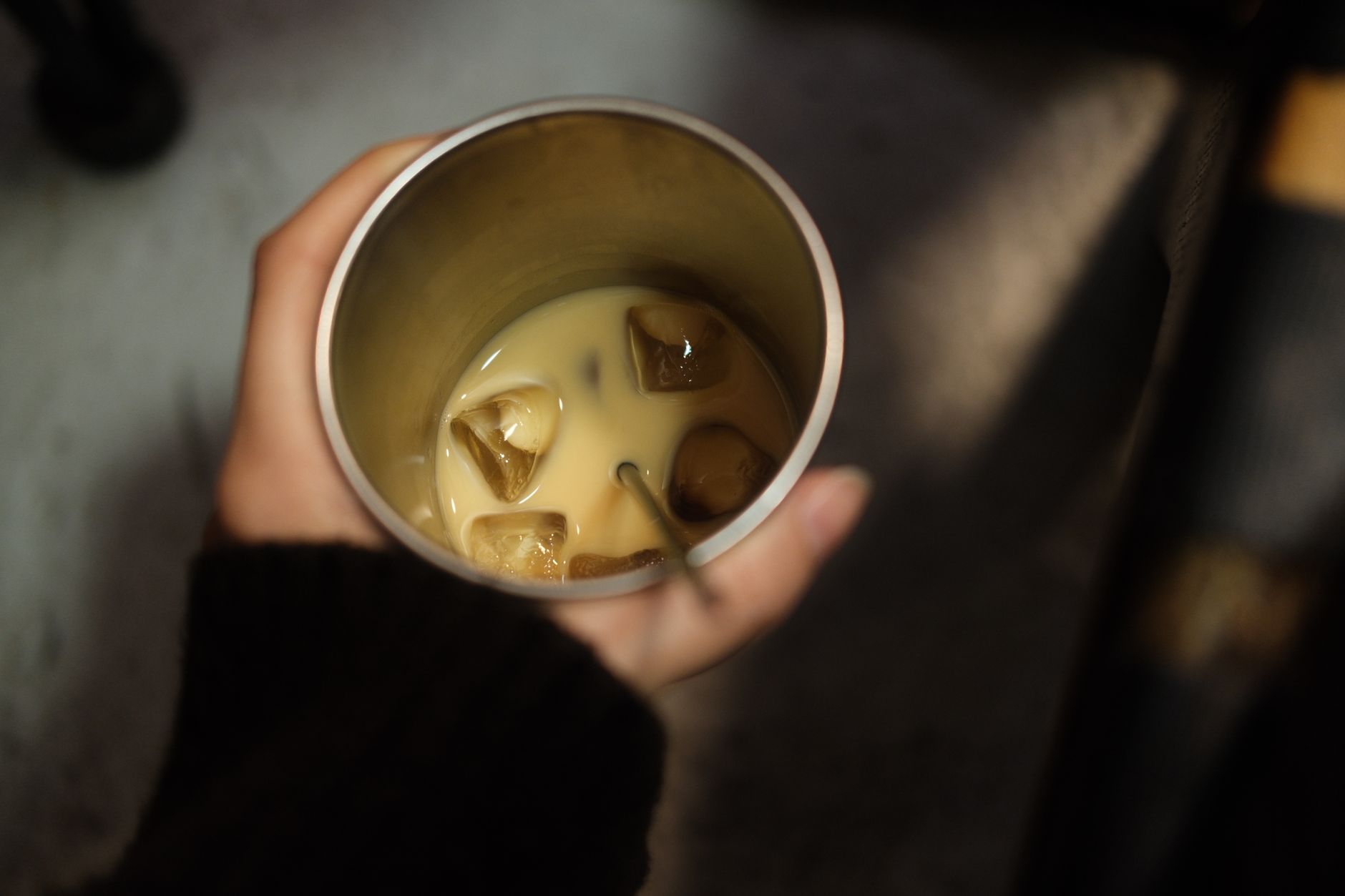 Hand holding a cup of iced coffee with milk, providing a cozy afternoon vibe.