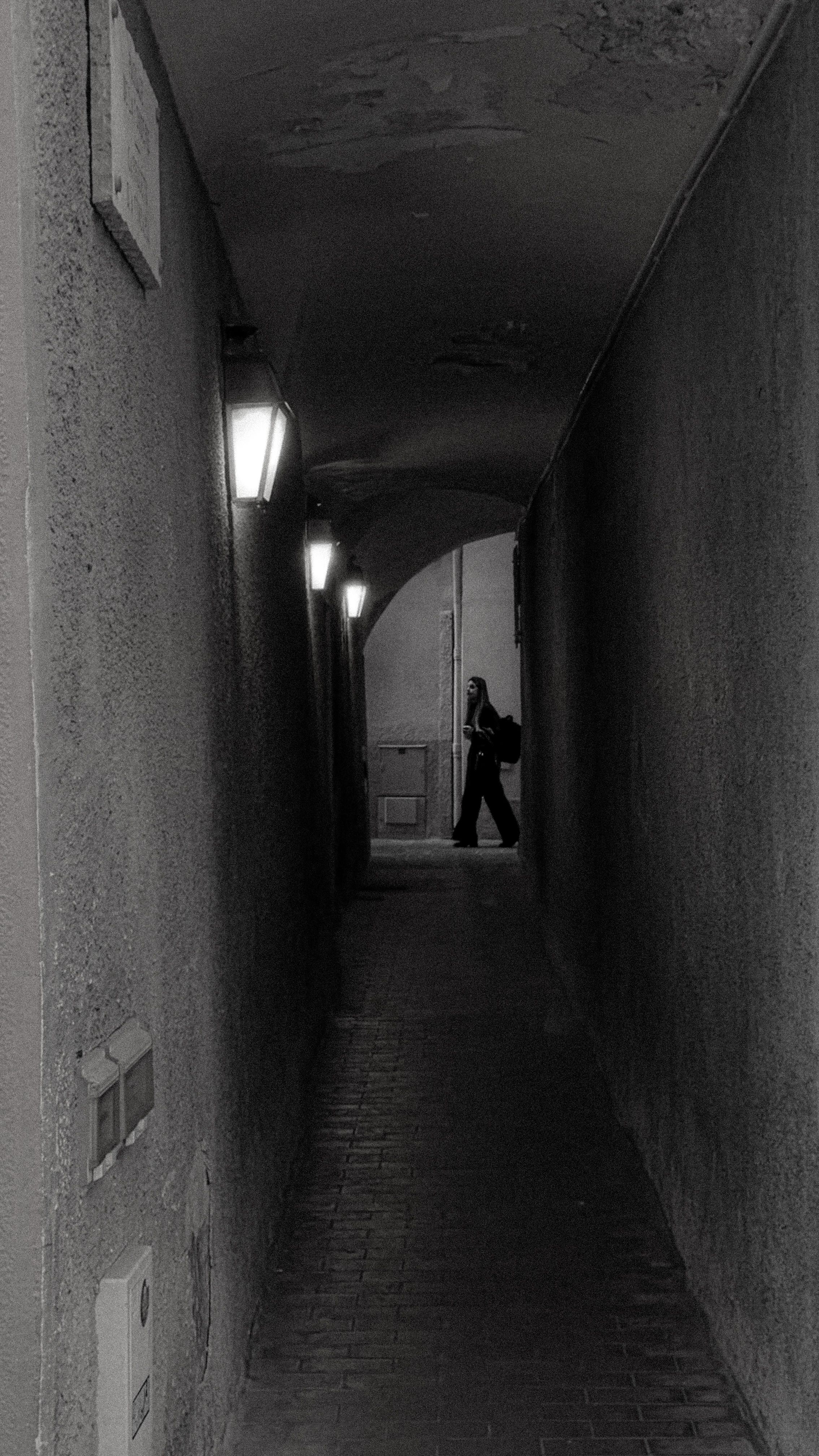 Black and white photo of a lone figure walking in a narrow alley, creating a mysterious mood.