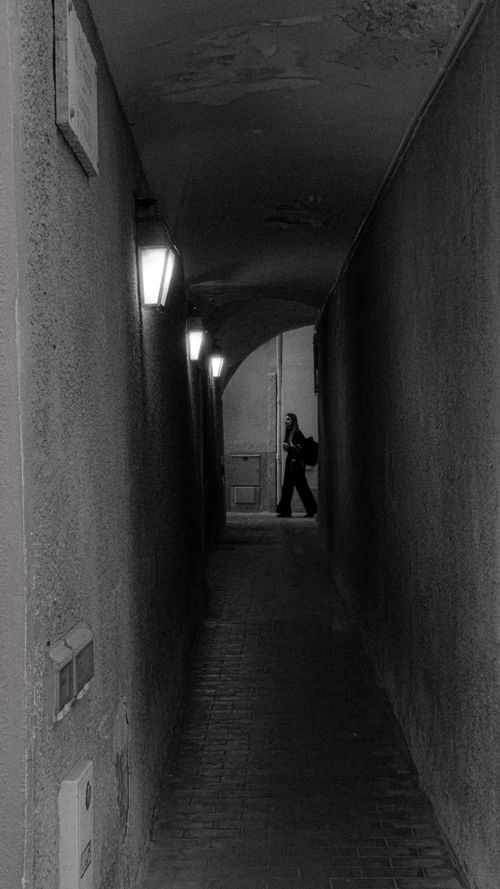 Free Black and white photo of a lone figure walking in a narrow alley, creating a mysterious mood. Stock Photo