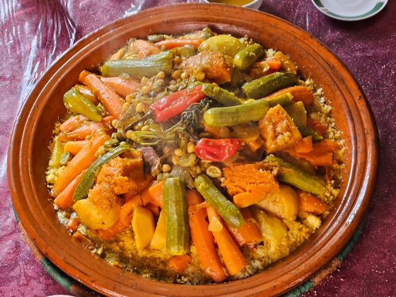 Couscous in a terracotta dish topped with zucchini, carrots, pumpkin, peppers and chickpeas