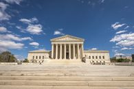 Front view of the United States Supreme Court building on a sunny day with blue sky and clouds.