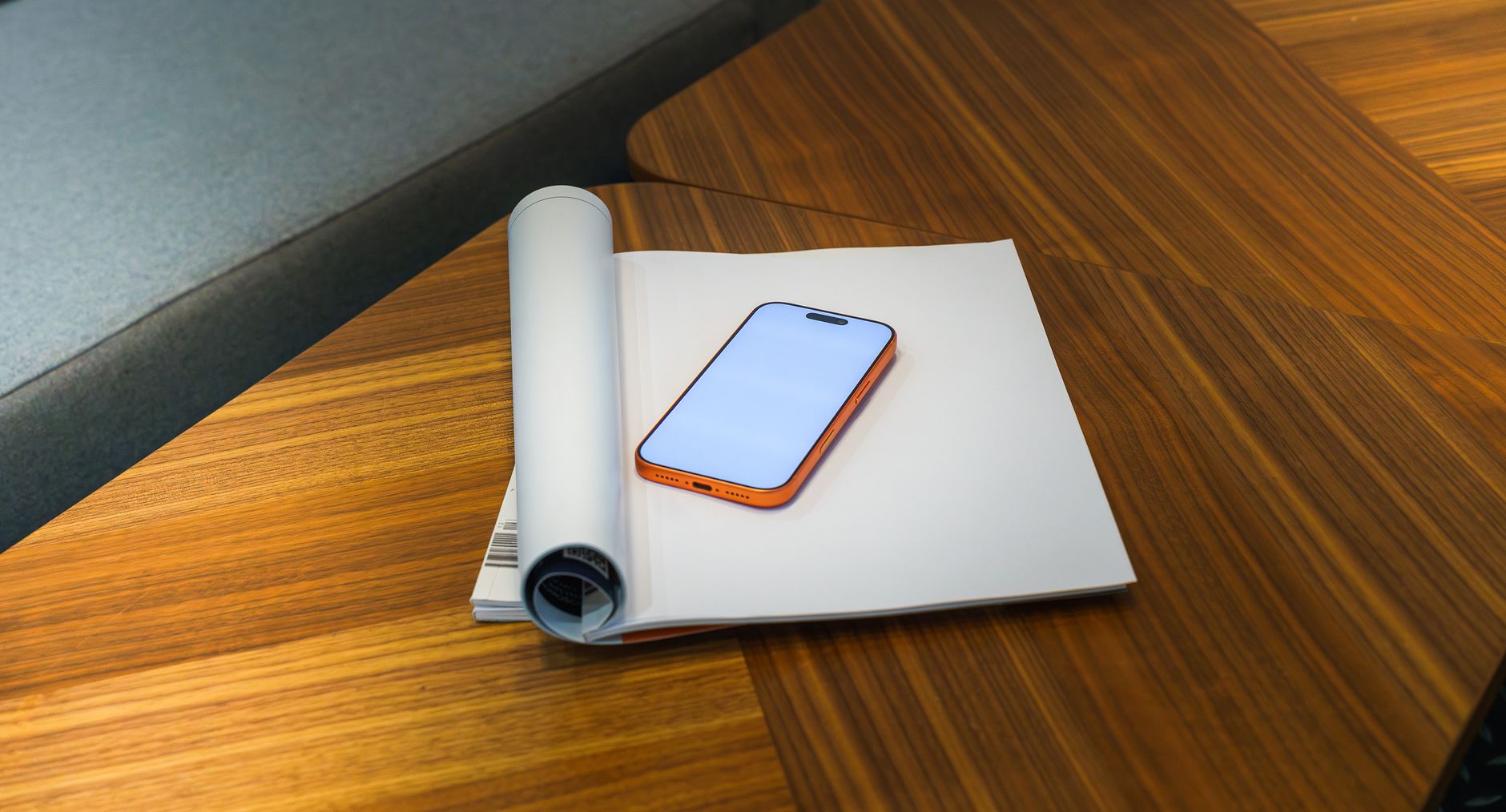 A stylish smartphone with an orange case lies on papers on a wooden desk, perfect for tech and lifestyle contexts.