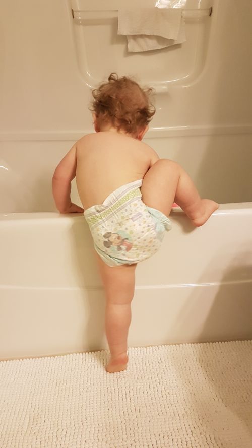 Free A cute toddler attempts to climb into a bathtub, showcasing curiosity and adventure. Stock Photo
