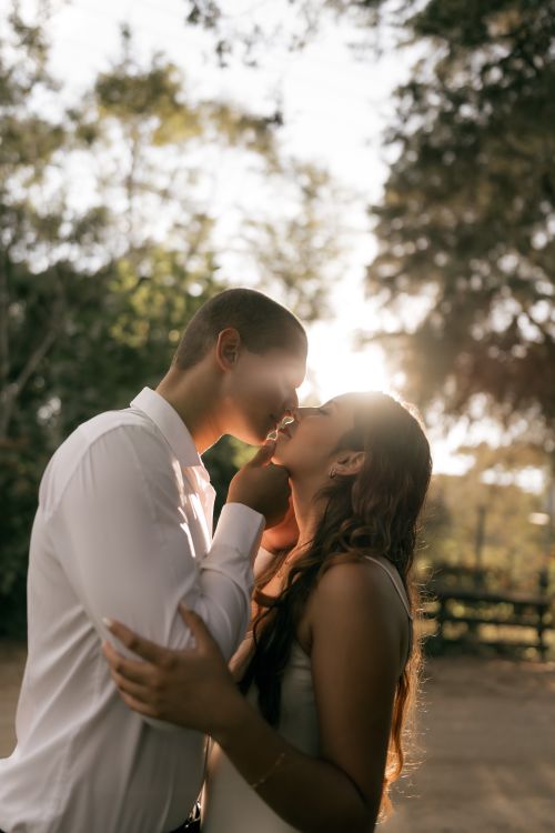 Free A couple shares a romantic kiss at sunset in a beautiful outdoor setting. Stock Photo