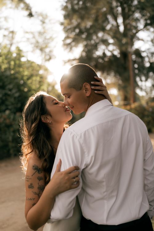 Free A couple shares a romantic kiss outdoors, bathed in warm sunlight, symbolizing love and connection. Stock Photo