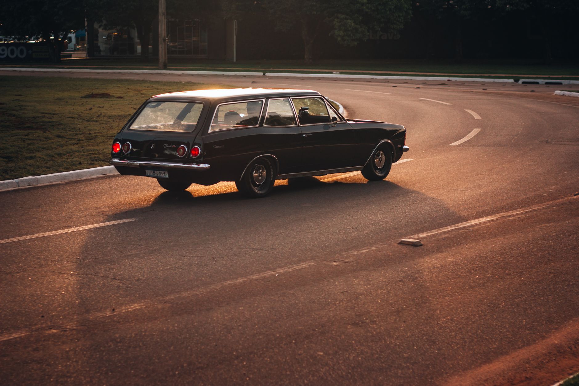 A vintage car driving on an empty road during golden hour, highlighting its classic design.