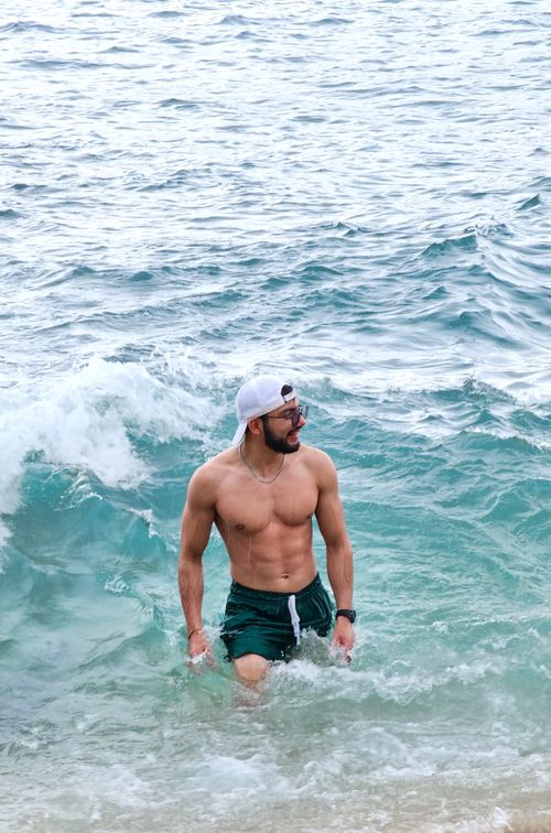 Free Man in swim trunks with a cap enjoying ocean waves, showcasing summer and leisure vibes. Stock Photo