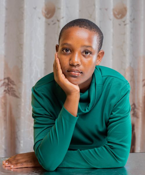 Free A young woman in a green top, resting her face on her hand, gazes thoughtfully indoors. Stock Photo