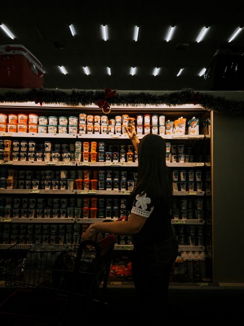 Free A woman shopping at a grocery store, reaching for an item on a shelf. Stock Photo