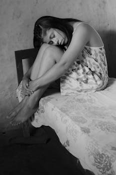 一个穿着花卉连衣裙的女人若有所思地坐在灰色房间的床上