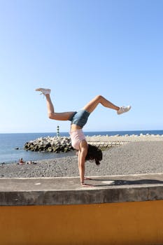 阳光明媚的马德拉海滩上，一位健康的女性在做倒立，展示着她的力量和灵活性