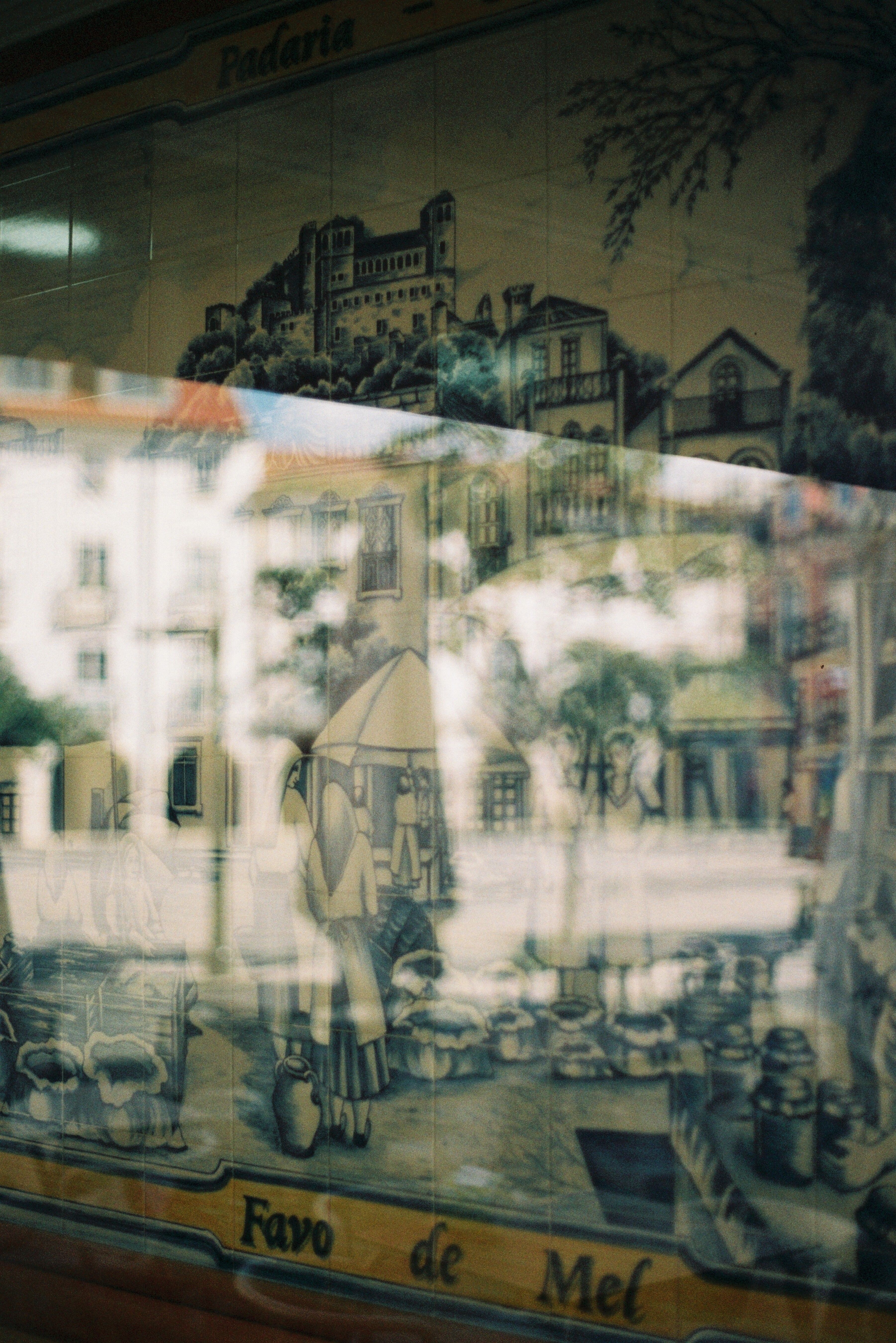 A vintage mural's reflection captures traditional Portuguese tile art in a Leiria storefront window.