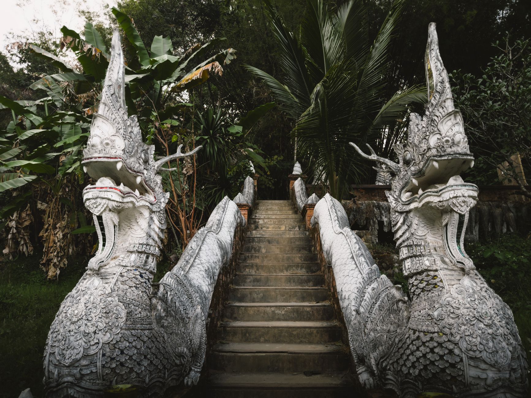 Intricate stone naga sculptures guarding a staircase in a lush jungle setting, evoking spiritual and mystical themes.