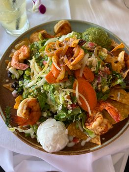 Delicious shrimp nachos topped with fresh vegetables, cheese, guacamole, and sour cream.