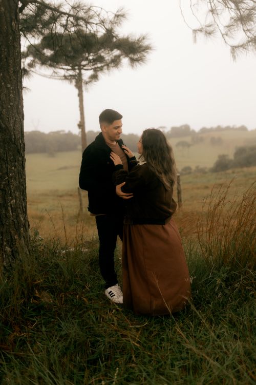 Free A couple stands embracing by a tree in a misty forest setting, evoking romance and nature's tranquility. Stock Photo