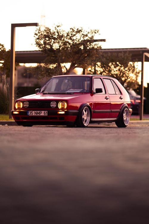 Free A red Volkswagen Golf MK2 parked outdoors during a beautiful sunset, reflecting light on its classic body. Stock Photo