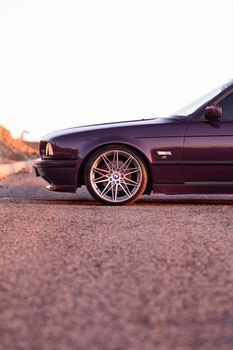 A detailed side view of a vintage car's wheel and body on a road during sunset.