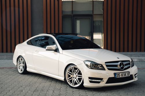 Free A polished white Mercedes-Benz coupe parked in front of a modern building facade. Stock Photo