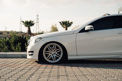 Free Side view of a white luxury car parked on a sunny day with palm trees in the background. Stock Photo