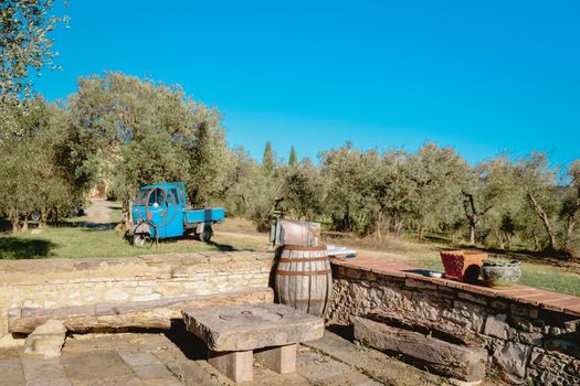 Charming scene of a Tuscan olive grove featuring a blue three-wheeler and rustic stone seating.