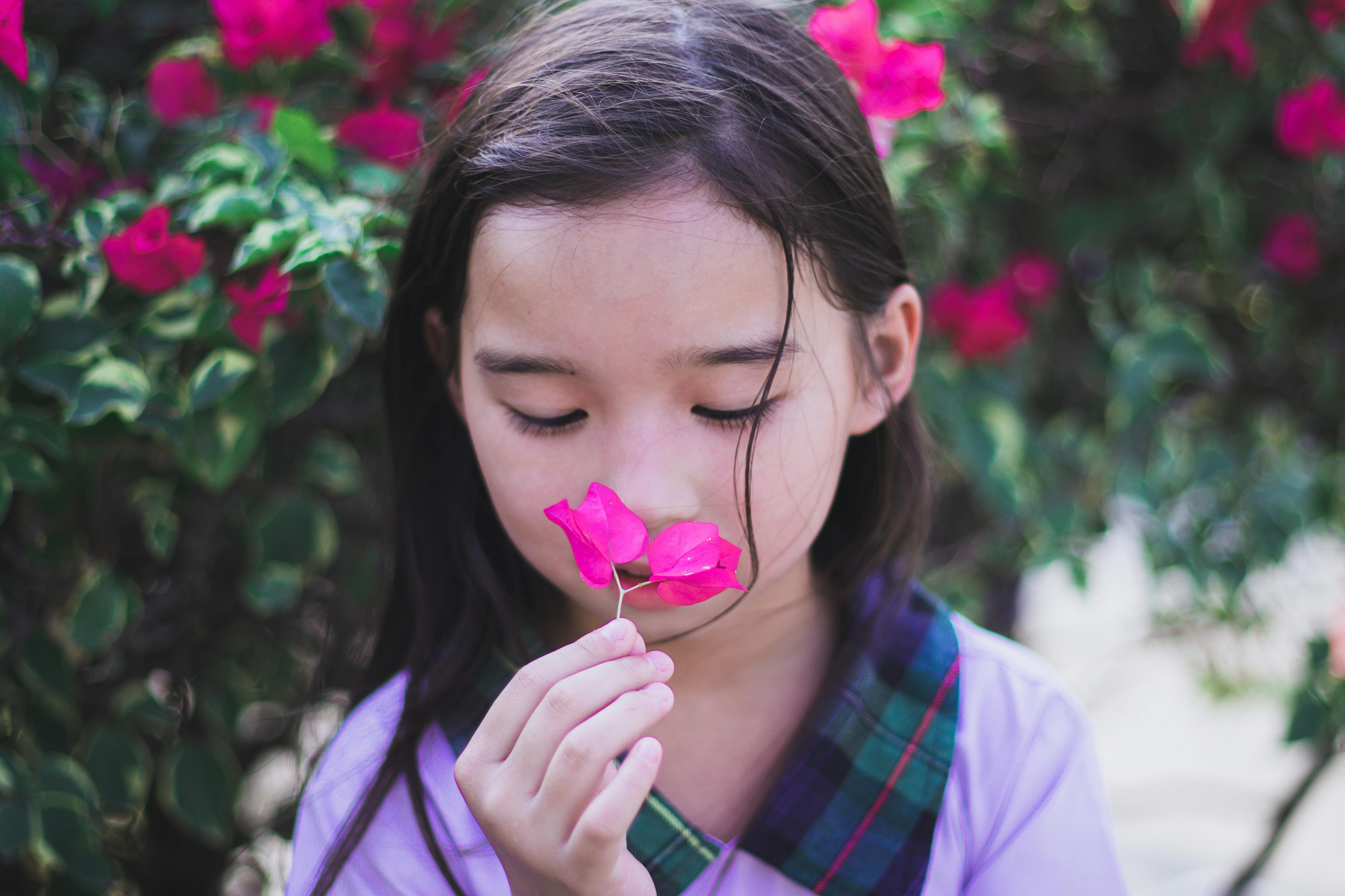 girl in purple top holding while smelling pink flower