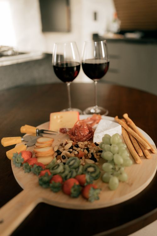 Free A stylish charcuterie board with assorted cheeses, fruits, and two glasses of red wine on a table. Stock Photo