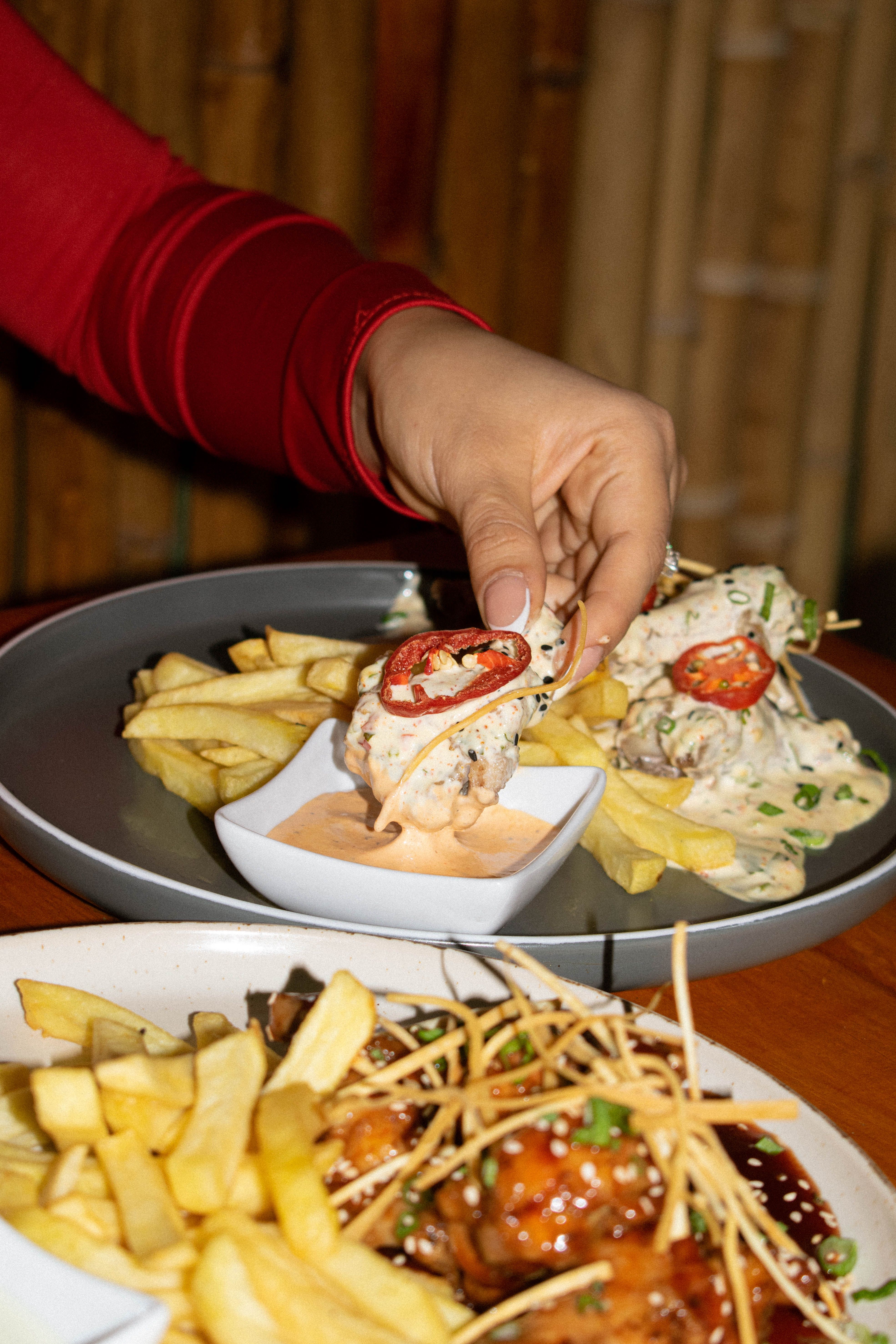 Hand picking a tasty chicken piece with fries and creamy dipping sauce in a cozy setting.