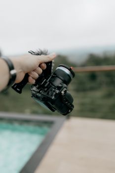 A photographer's hand holding a DSLR camera with a blurred outdoor background