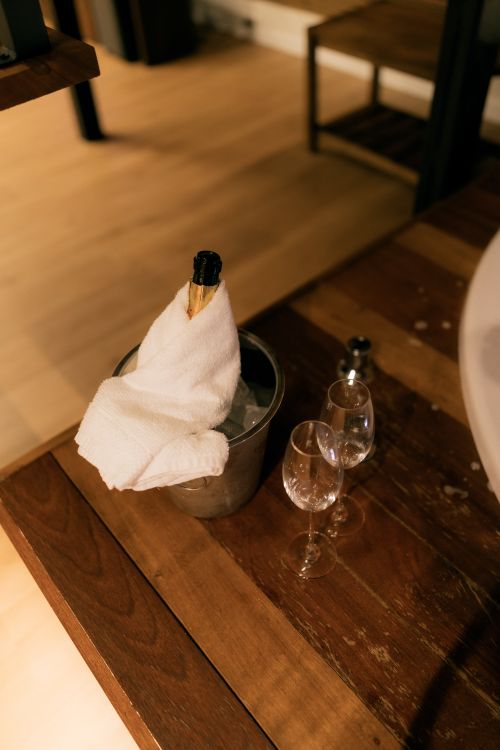 Free A champagne bottle wrapped in a towel rests in an ice bucket with wine glasses on a wooden table. Stock Photo