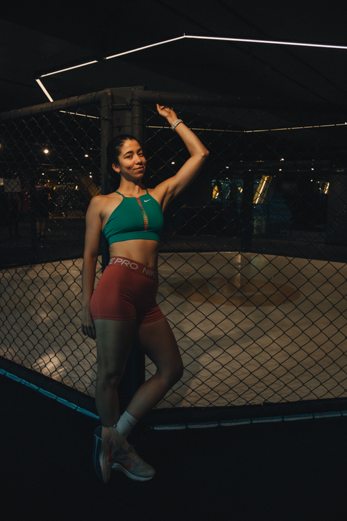 Free Fit woman in sportswear posing confidently by a cage in a gym, nighttime setting. Stock Photo
