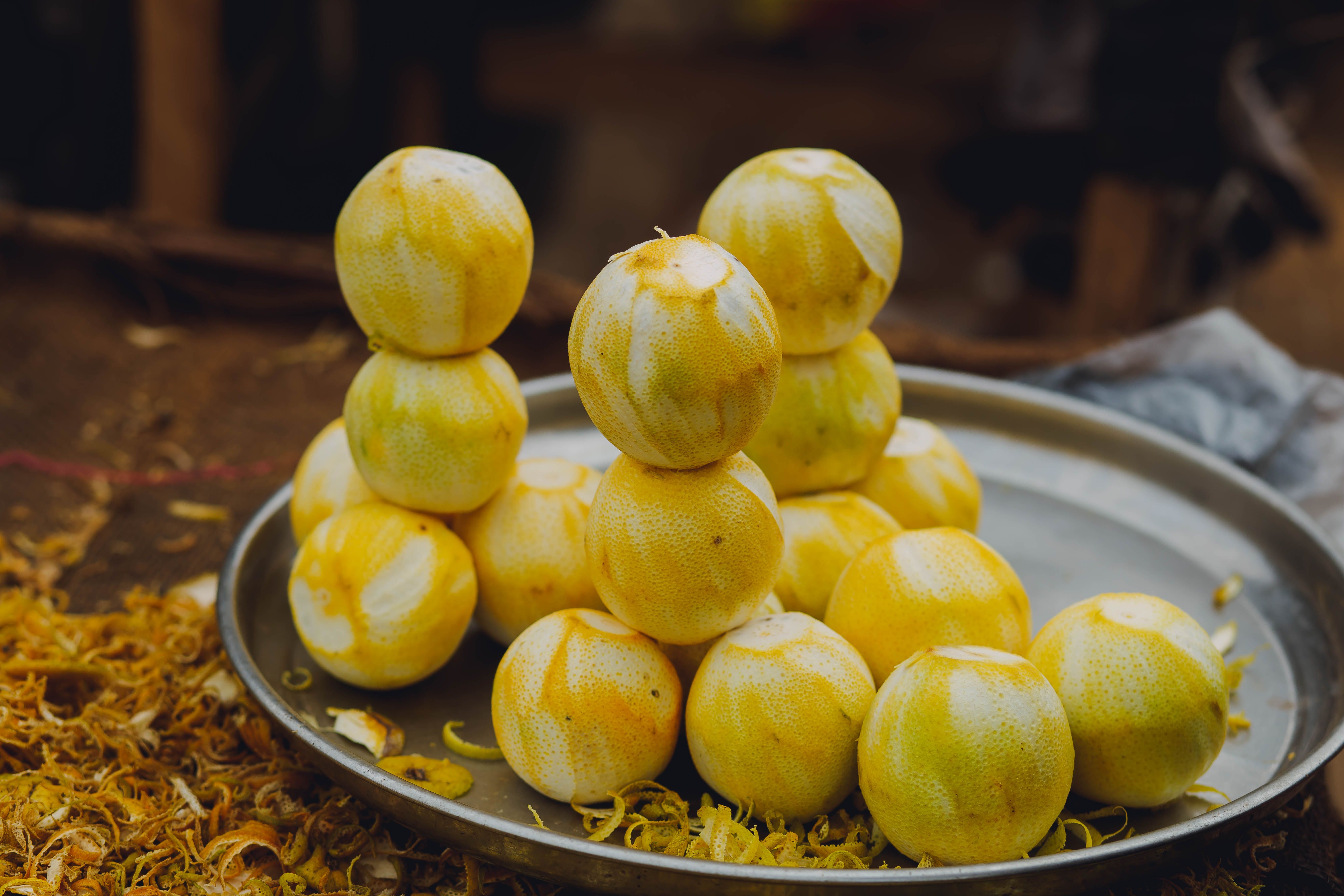 A close-up of stacked fresh lemons on a metal tray with lemon peels, showcasing vibrant yellows.