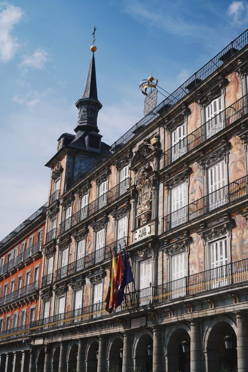 Free View of Plaza Mayor in Madrid, showcasing its detailed architecture and vibrant flags on a clear day. Stock Photo