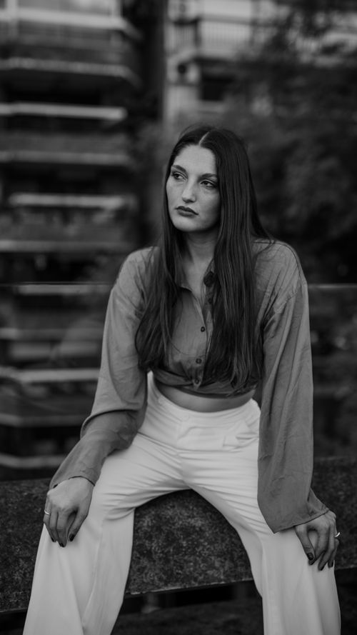 Free A thoughtful young woman sitting outdoors in a black and white portrait. Stock Photo
