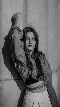 Stylish black and white portrait of a woman leaning against a textured wall, evoking elegance.