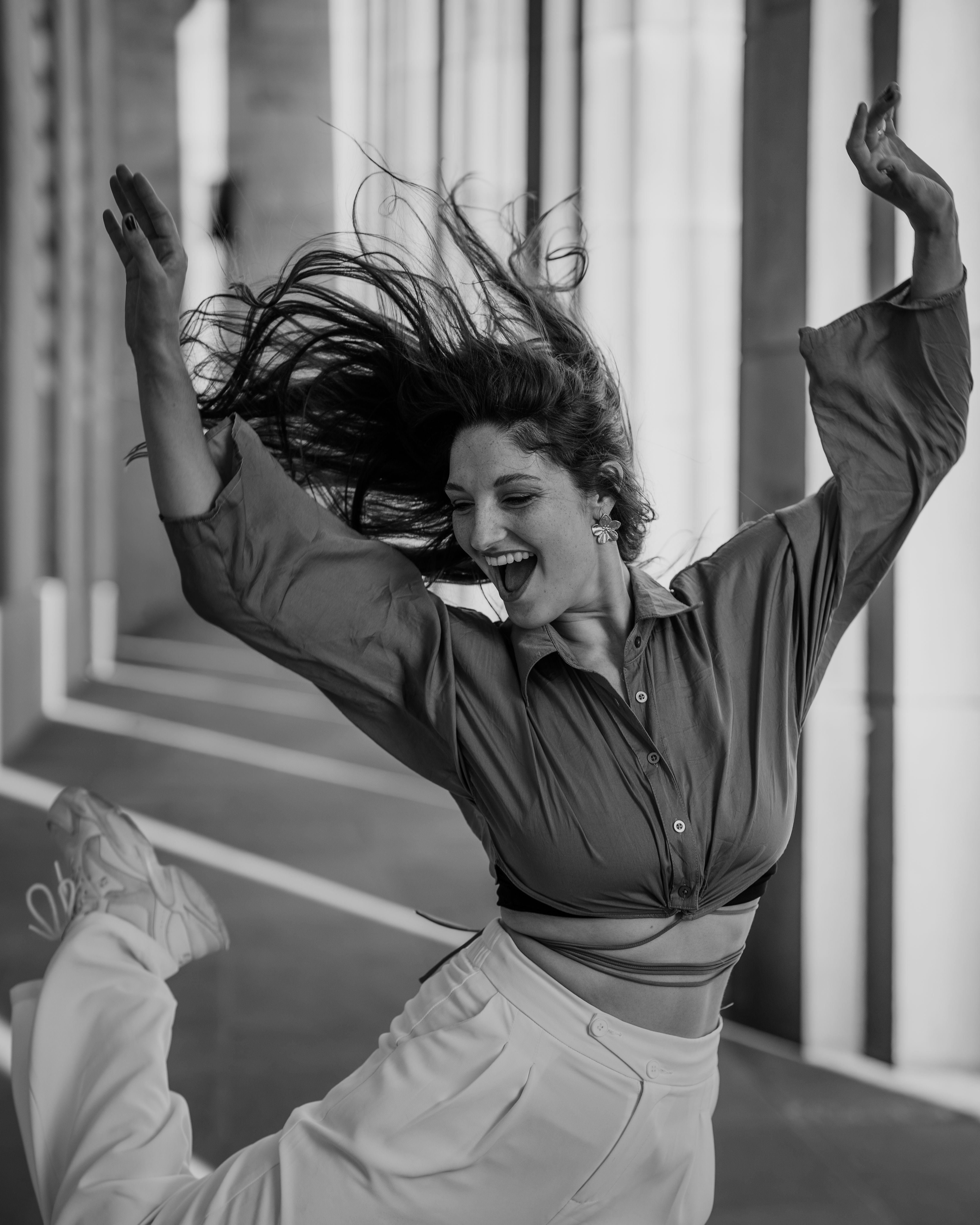 A woman joyfully dances with arms raised in an urban corridor.
