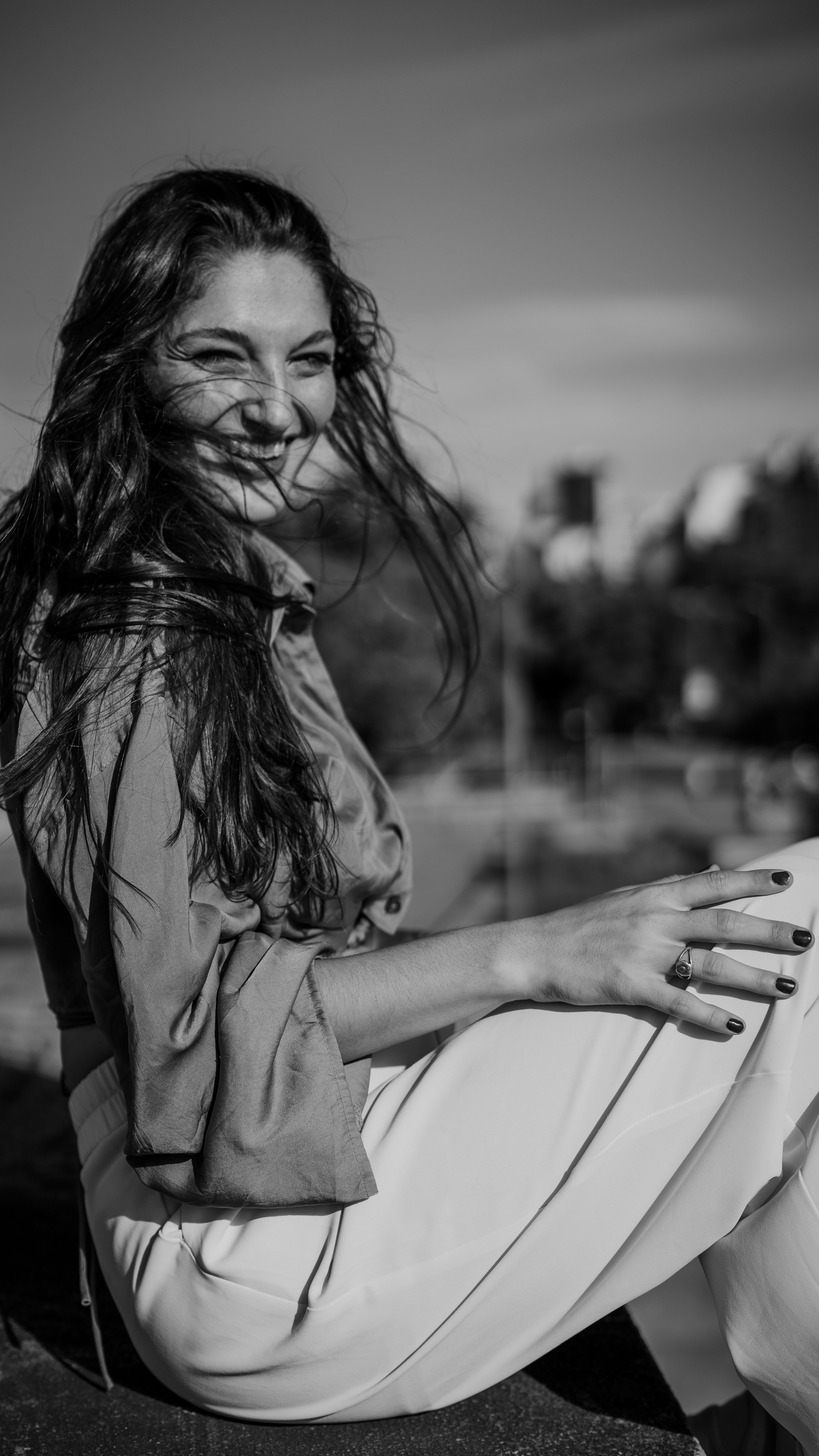 Outdoor black and white portrait of a smiling woman seated casually.
